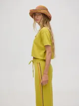 Pantalón de punto color verde oliva, confeccionado en algodón, con corte holgado, pierna ancha y tiro alto. Cuenta con pretina elástica con cordón de ajuste y una línea lateral a contratono en color naranja.