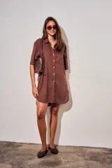 Vestido camisero corto de color marrón, con mangas cortas, cuello camisero, cierre frontal de botones y un bolsillo ojal en el pecho.