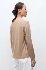 Remera de manga larga color tostado melange, con cuello redondo y detalle de botones metálicos en los puños.