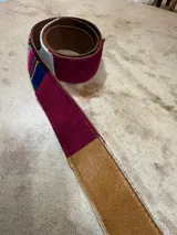 Cinturón de cuero marrón combinado con inserciones de gamuza, pelo vacuno y tejido tipo aguayo de colores. Cuenta con hebilla metálica rectangular envejecida.