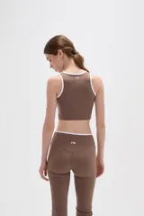 Top deportivo sin mangas, color camel, con cuello redondo y detalles de ribete en color blanco. Presenta un diseño al cuerpo con costuras decorativas en el bajo.