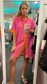 Camisola de lino fucsia con detalles en color naranja en cuello, solapa de botones, bordes de mangas y ruedo. De corte holgado, manga corta y cierre frontal con botones.