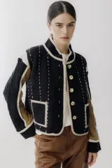 Chaqueta de punto con diseño color block en negro, beige y marrón. Presenta cuello redondo, cierre frontal con botones grandes, bolsillos frontales y detalles de costuras decorativas verticales en color claro.