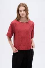 Blusa de viscosa color marrón rojizo, con diseño holgado, cuello a la base, mangas cortas y detalle de bordado floral en tono sobre tono.