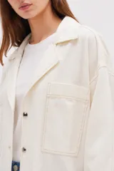 Sobrecamisa de lino y viscosa color marfil, con cuello solapa, mangas tres cuartos anchas, bolsillos frontales con solapa y cierre de botones oscuros.