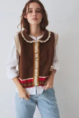 Chaleco de punto color chocolate con cuello bebé tejido en color crema, cierre frontal con botones, detalle de bolsillo pequeño y franjas decorativas en la parte inferior en tonos rojo, marrón y mostaza.