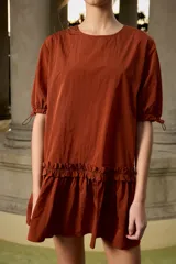 Vestido corto de nylon color terracota, con cuello redondo, mangas cortas abullonadas con cordones ajustables y detalle de volados en la parte inferior.