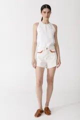 Short de denim color blanco roto, tiro alto, con terminación deshilachada en el ruedo. Presenta detalles de crochet en color rojo en los bordes de los bolsillos delanteros.