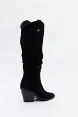 Bota texana de caña alta confeccionada en gamuza negra, con punta fina y taco cuadrado de 5 cm. Presenta un diseño con efecto arrugado en la caña y cierre lateral para facilitar su colocación.