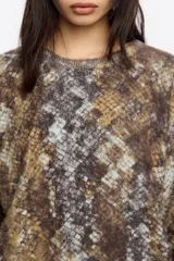 Jersey de punto con textura suave, cuello redondo y mangas largas con puños ajustados. Presenta un diseño de estampado animal print en tonos marrones, grises y azulados.
