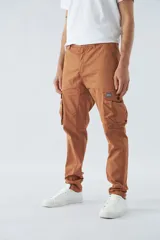 Pantalón cargo color beige, corte slim, con cierre y botón en la cintura, pasacintos, bolsillos cargo con botones y sin puños.