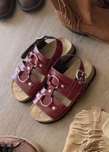 Sandalias planas color rojo cereza, estilo gladiador con tiras anchas y múltiples hebillas metálicas circulares. Cuentan con plantilla anatómica y suela antideslizante.