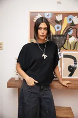 Blusa negra de corte holgado con mangas cortas tipo murciélago y cuello redondo. Confeccionada en tela con textura sutil.