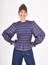 Blusa de mangas largas abullonadas con puños elásticos y cuerpo con diseño fruncido tipo nido de abeja. Presenta un estampado de cuadros escoceses en tonos azules, verdes y rojos.