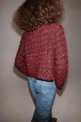 Chaqueta de punto con textura y estructura de tweed, en combinación de rojo y negro. Cuenta con cuello redondo, manga larga, bolsillos delanteros de plastrón y cierre frontal con botones metálicos dorados.