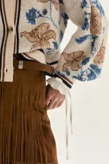 Cardigan de tejido de punto color crudo con diseño de jacquard floreado en tonos azules y marrones. Presenta cuello en V, cierre frontal con botones y ribetes a rayas en cuello, puños y bajo.
