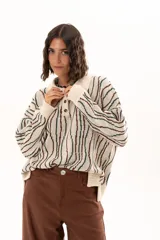 Buzo de tejido de punto con diseño de rayas verticales onduladas en tonos verde y marrón sobre base color crudo. Presenta cuello tipo polo con cierre frontal de botones y mangas largas con puños acanalados.