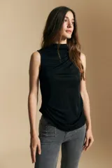 Top sin mangas de color negro con cuello alto y diseño drapeado en el frente. Confeccionado en una tela suave con acabado levemente satinado y silueta fluida.