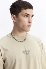 Remera de manga corta color beige, con escote redondo y estampado frontal con la palabra "Surreal" en tipografía cursiva.