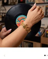 Pulsera de malla metálica con baño de oro, con dijes de guitarra y auriculares, y detalles de circonias en los extremos.