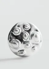 Aros circulares plateados de diseño metálico texturizado con apliques de perlas y cierre de clip.
