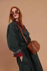 Bandolera de diseño rectangular en color suela, confeccionada en material sintético. Cuenta con un asa superior fija, correa larga ajustable y extraíble, y dos bolsillos frontales con cierre metálico, uno de ellos con diseño superpuesto. Presenta el logo de la marca grabado en el frente.