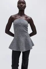 Top strapless de tejido de punto gris, ajustado al cuerpo con peplum acampanado en la parte inferior. Está adornado con perlas y pequeños cristales distribuidos por toda la prenda.