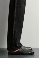 Zueco de vestir para hombre confeccionado en piel de color negro, con horma redonda, diseño destalonado y suela plana a tono.