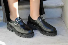 Zapato tipo mocasín de cuero color negro, con hebilla metálica plateada y suela track.