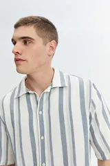 Camisa de manga corta oversize en tejido rústico, con diseño de rayas verticales celestes y blancas, cuello clásico y cierre frontal de botones.