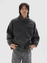 Buzo de sherpa color gris oscuro, con cuello alto y medio cierre frontal. Presenta un bolsillo ojal en el pecho con cierre y bolsillos laterales. Cuenta con cordón regulable en el ruedo para un ajuste personalizado.