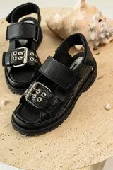 Sandalias negras de cuero con diseño de plataforma dentada, tiras ajustables con hebillas metálicas y detalle de tachas plateadas en el lateral de la suela.