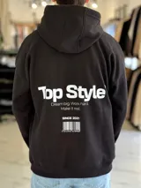 Canguro negro oversize con capucha y gran estampado blanco en la espalda con el texto "Top Style", "Dream big. Work hard. Make it real.", "SINCE 2021" y un código de barras.