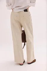 Pantalón de lino lavado color beige, de calce recto y diseño relajado. Presenta cintas de lino desflecadas aplicadas en los laterales con pespunte central, pretina con botón metálico, bolsillos delanteros y traseros.