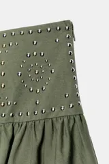 Falda de tiro medio confeccionada en algodón, con cintura ancha decorada con tachas metálicas y bajo asimétrico con caída fluida. Cuenta con cierre lateral oculto.