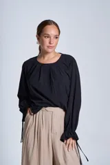 Blusa de manga larga color rosado, con cuello redondo y puños elásticos con volados y lazos decorativos. Presenta un diseño holgado con frunces en el escote.