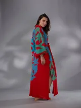 Kimono largo de algodón texturado con estampado vegetal en tonos rojo, azul y verde. Cuenta con mangas amplias, cinto independiente para ajustar a la cintura, bolsillos laterales y aberturas laterales en el dobladillo con detalles de flecos.