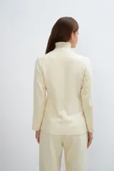 Chaqueta corta color beige, entallada, con escote en V, manga larga y bolsillos escondidos. Cierre frontal con lazo fijo. Confeccionada en lana fina sin teñir. Diseño exclusivo de Don Baez.