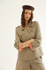 Chaqueta corta de inspiración motoquera color beige, confeccionada en lino fantasía, sin forro, con cierres decorativos, broches de presión y bolsillos delanteros funcionales. Presenta detalle bajo el cuello y en vueltas de mangas en color mostaza y rayas.