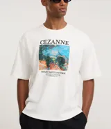 Remera boxy de algodón color blanco, con cuello redondo y mangas cortas. Presenta un estampado artístico inspirado en la obra "Mount Sainte-Victoire" de Paul Cézanne.