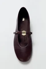Zapato tipo bailarina de cuero color bordó, con tira ajustable en el empeine, detalle metálico y punta redonda.