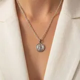 Dije circular de plata 925 con relieve de la Virgen Stella Maris. Presenta un diseño detallado con acabado envejecido que resalta la figura central y los rayos circundantes.