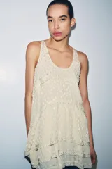 Vestido corto de viscosa color beige con diseño de jacquard, escote redondo y manga sisa. Presenta un diseño de paneles asimétricos con aplicaciones de abalorios decorativos en las costuras.