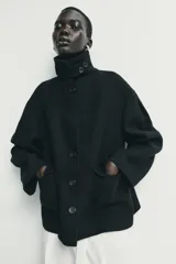Abrigo corto de paño con mezcla de lana, color negro. Presenta cuello subido con cierre de botones, manga larga y dos bolsillos de plastrón con solapa en el frente. Cierre frontal con botones.