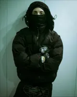 Campera puffer negra con capucha, cierre frontal con botones a presión y cordones ajustables en la cintura. Presenta un estampado gráfico circular con el número 27 en el pecho.