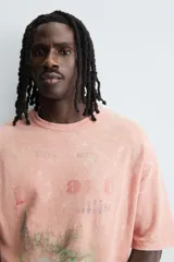 Camiseta de punto de algodón con corte boxy fit, cuello redondo y manga corta. Presenta un estampado frontal con diseño de paisaje y texto en tonos deslavados. La prenda tiene un efecto lavado que le da un aspecto envejecido e irregular.