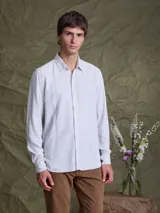 Camisa de manga larga en color blanco hueso, con cuello clásico y cierre frontal de botones. Confeccionada en tejido ligero de textura suave.