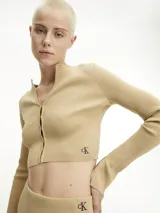 Sweater cárdigan de punto canalé color beige, de corte slim cropped y manga larga. Presenta cierre frontal con corchetes y logo bordado de Calvin Klein en el bajo.
