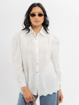 Camisa blanca de algodón con delicados bordados florales y líneas verticales sutiles, cuello camisero clásico y cierre frontal de botones.