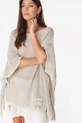 Blusa de punto estilo poncho en color beige, con diseño amplio, cuello redondo y aplique de etiqueta con el logo de la marca en el borde inferior.